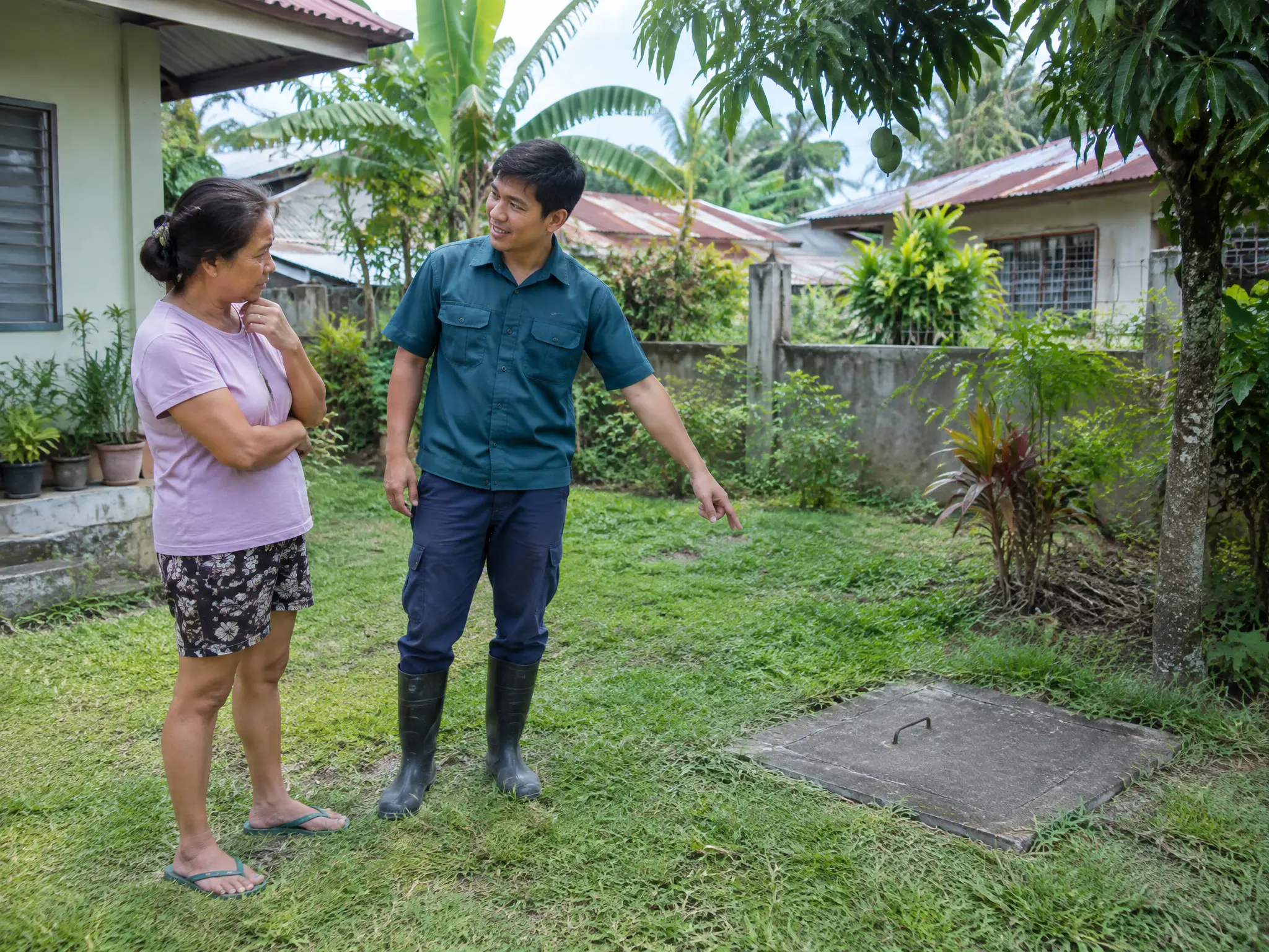 Manggagawa na sumasagot sa tanong ng may-ari ng bahay habang itinuturo ang takip ng pozo negro